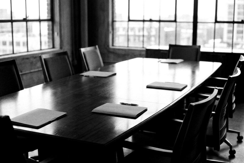Table de comité de direction vide après une réunion, dossiers et tableau de bord RH laissés sur la table, photographie noir et blanc