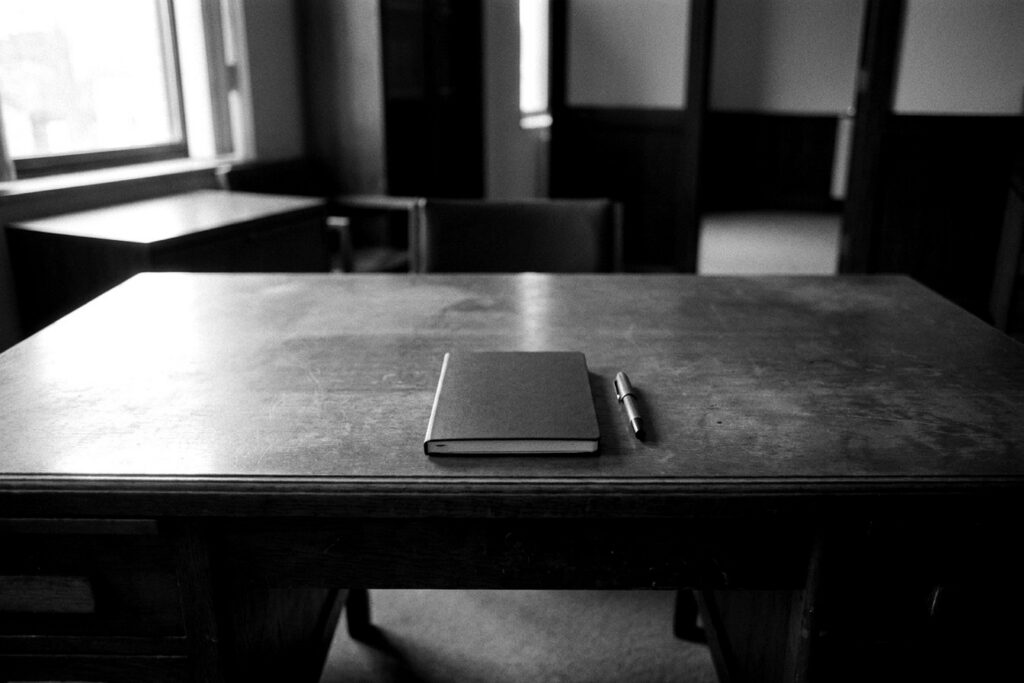 Bureau en bois massif avec un carnet fermé et un stylo, bureau vide en noir et blanc